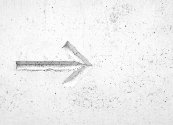 Uz pelēkbalta fona iegravēta bulta, kas rāda virzienu no kreisās uz labo pusi. 