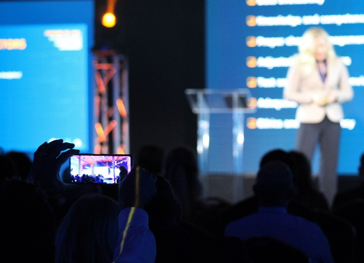 A person photographs a representative of Financial Intelligence Unit of Latvia, who is giving a presentation at a conference.
