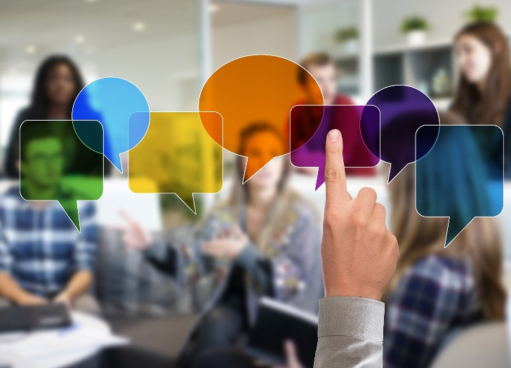 Grafiski attēloti dialoga logi ekrānā, fonā redzami cilvēki. Foto: pexels.com